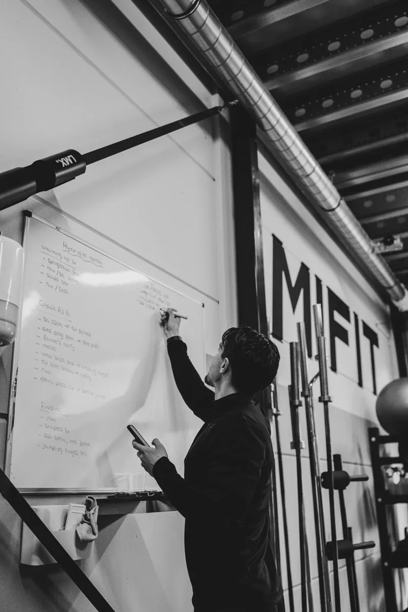 Een personal trainer schrijft een trainingsplan op het whiteboard in de studio